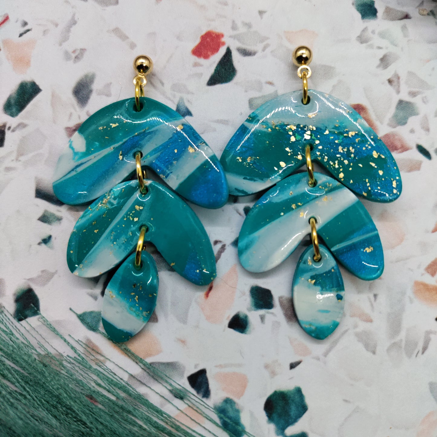 Teal and gold earrings on a textured white background