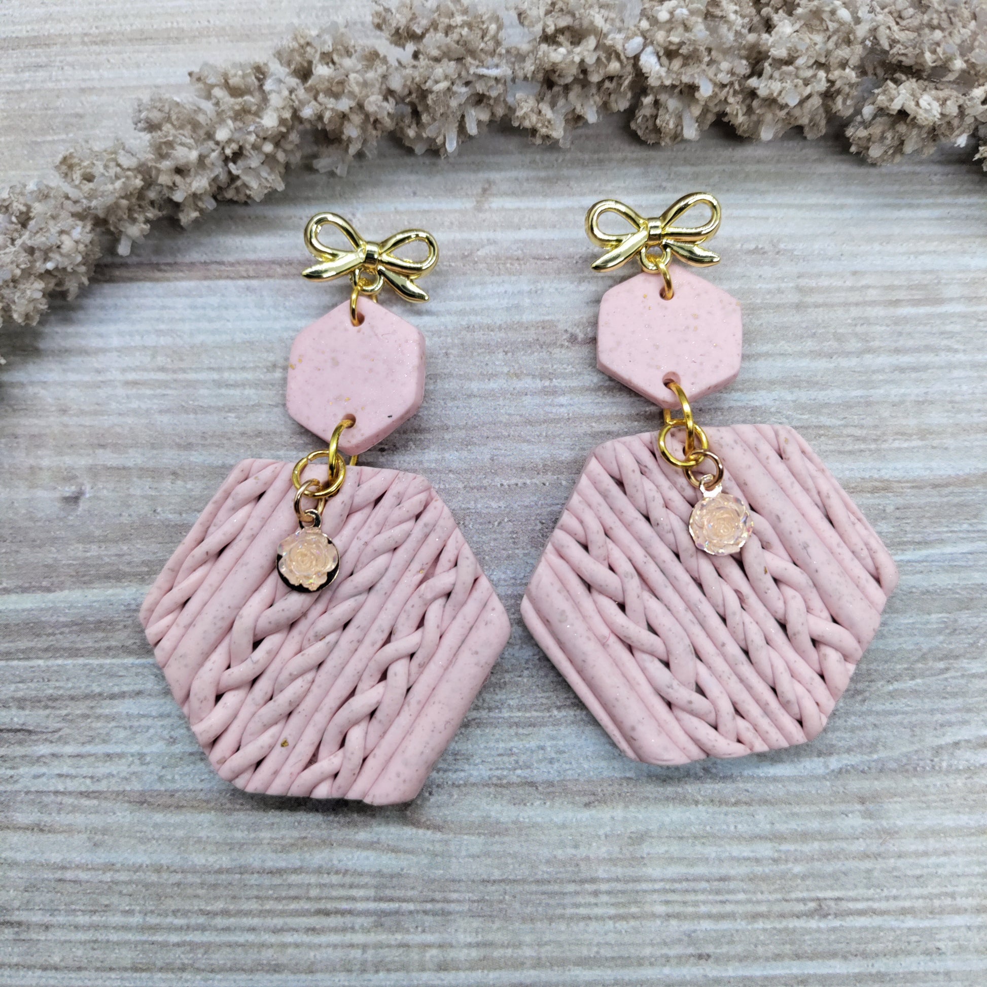 Pink earrings with gold accents on a textured surface