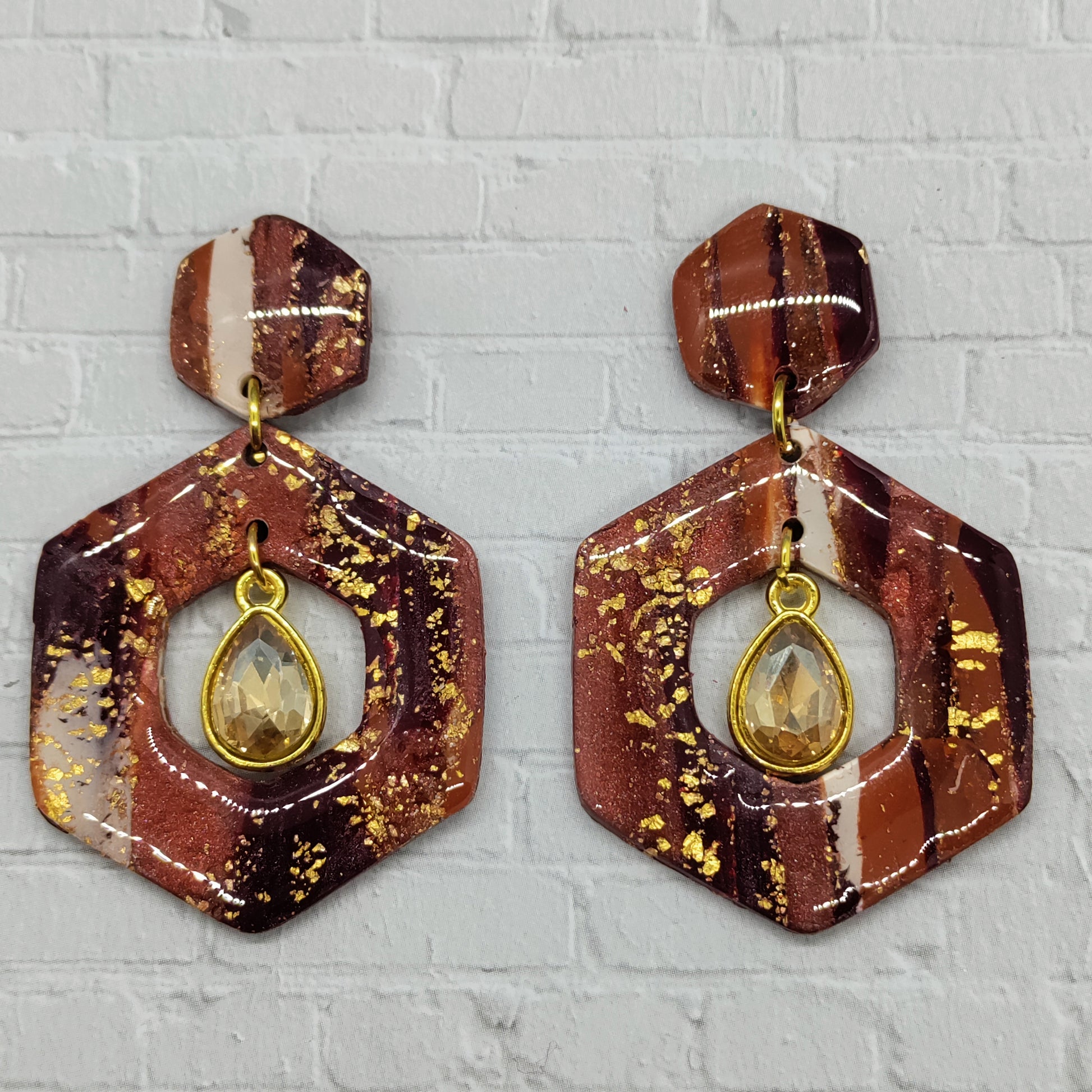 Hexagonal earrings with gold accents on a textured gray background
