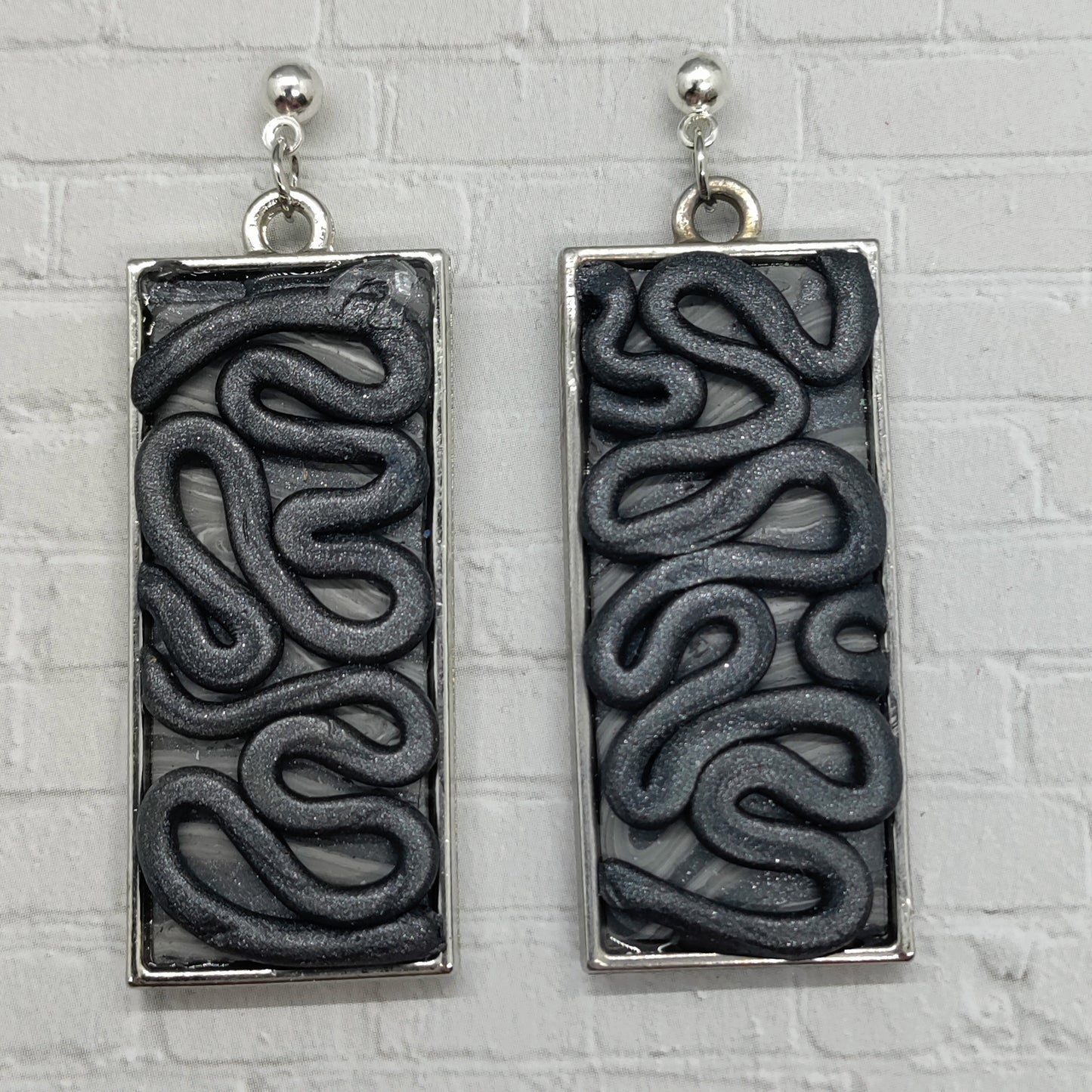 Pair of rectangular earrings with wavy pattern on a textured gray background
