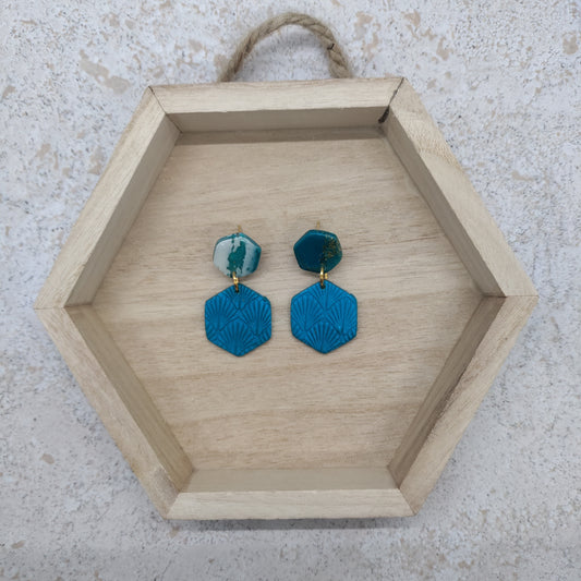 Hexagonal wooden tray with blue earrings on a textured surface