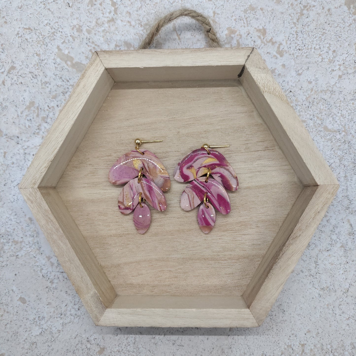 Pink floral earrings on a wooden hexagonal tray with a textured background