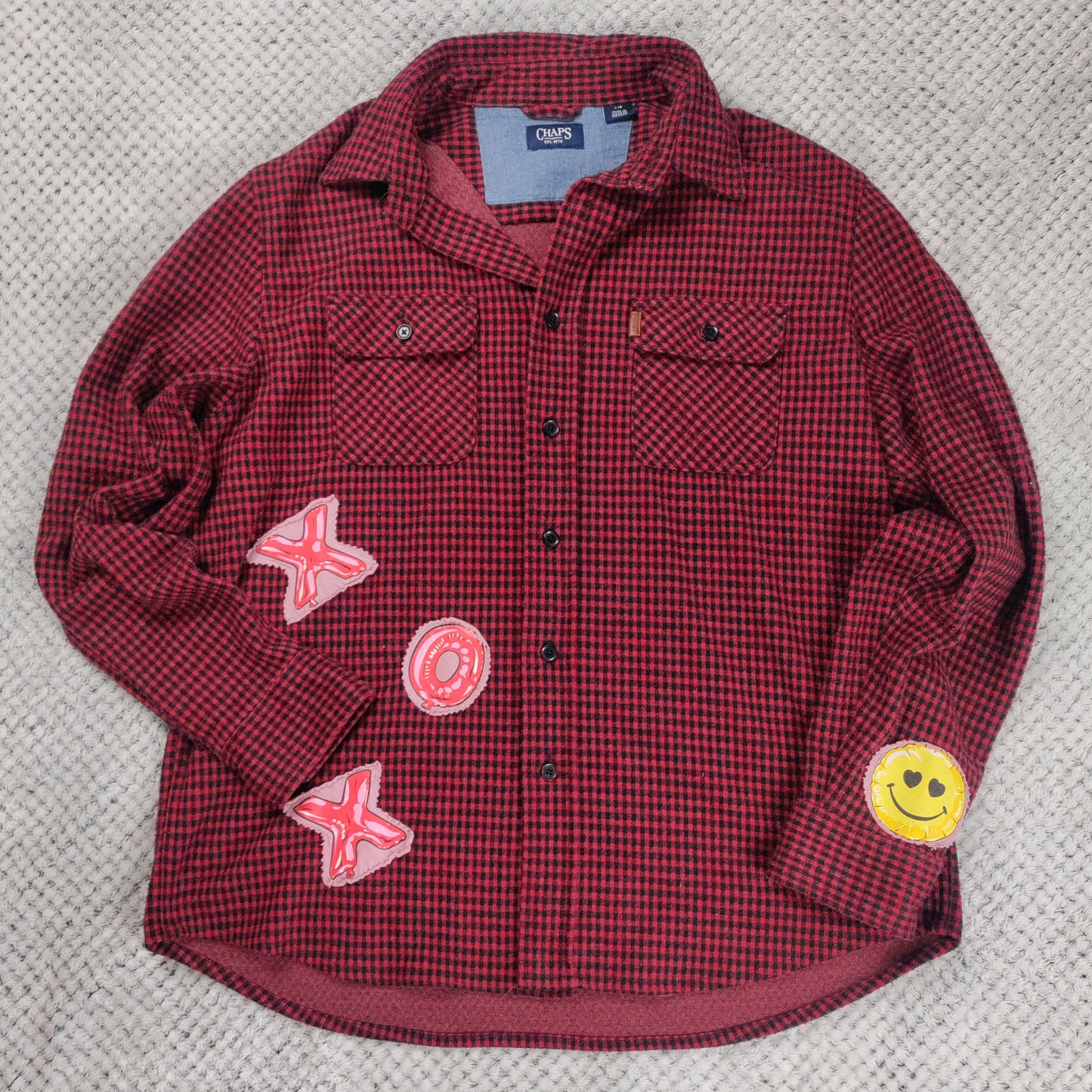 Red checkered shirt with patches on a textured gray surface