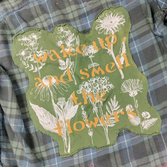 Green patch with floral design and text 'Wake up and smell the flowers' on a plaid shirt.
