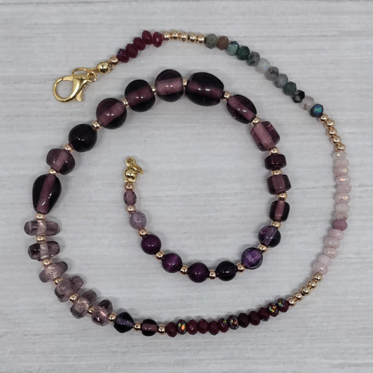 Beaded necklace with purple and gold accents on a light gray background