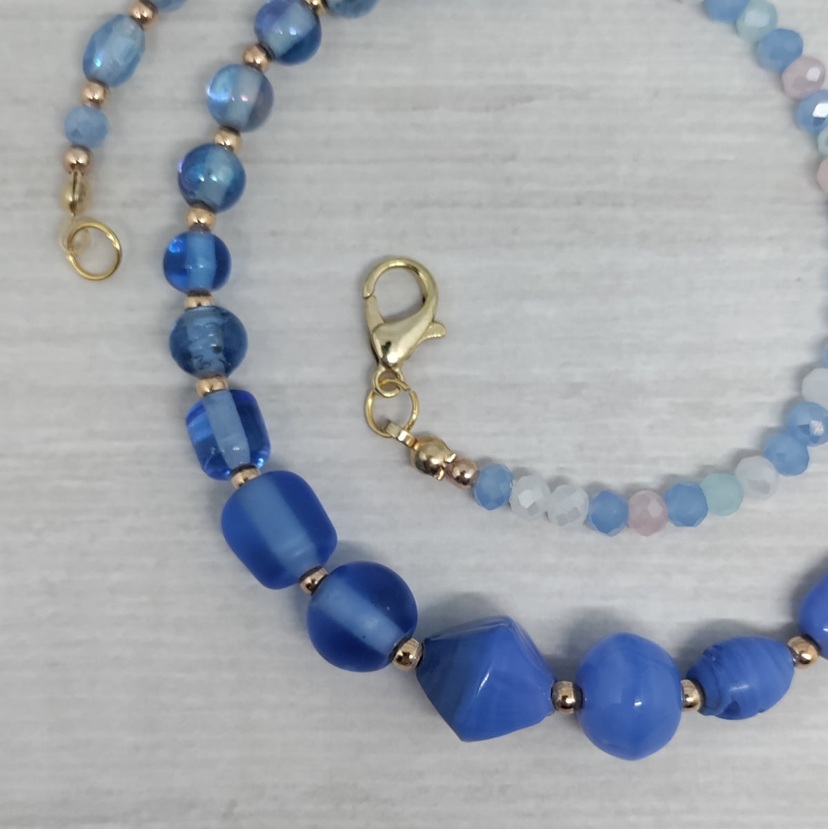 Blue beaded necklace with gold accents on a light gray background