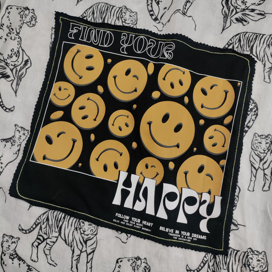A black bandana with yellow smiley faces and the words 'FIND YOUR HAPPY' laid flat on top of a white fabric featuring black animal sketches.