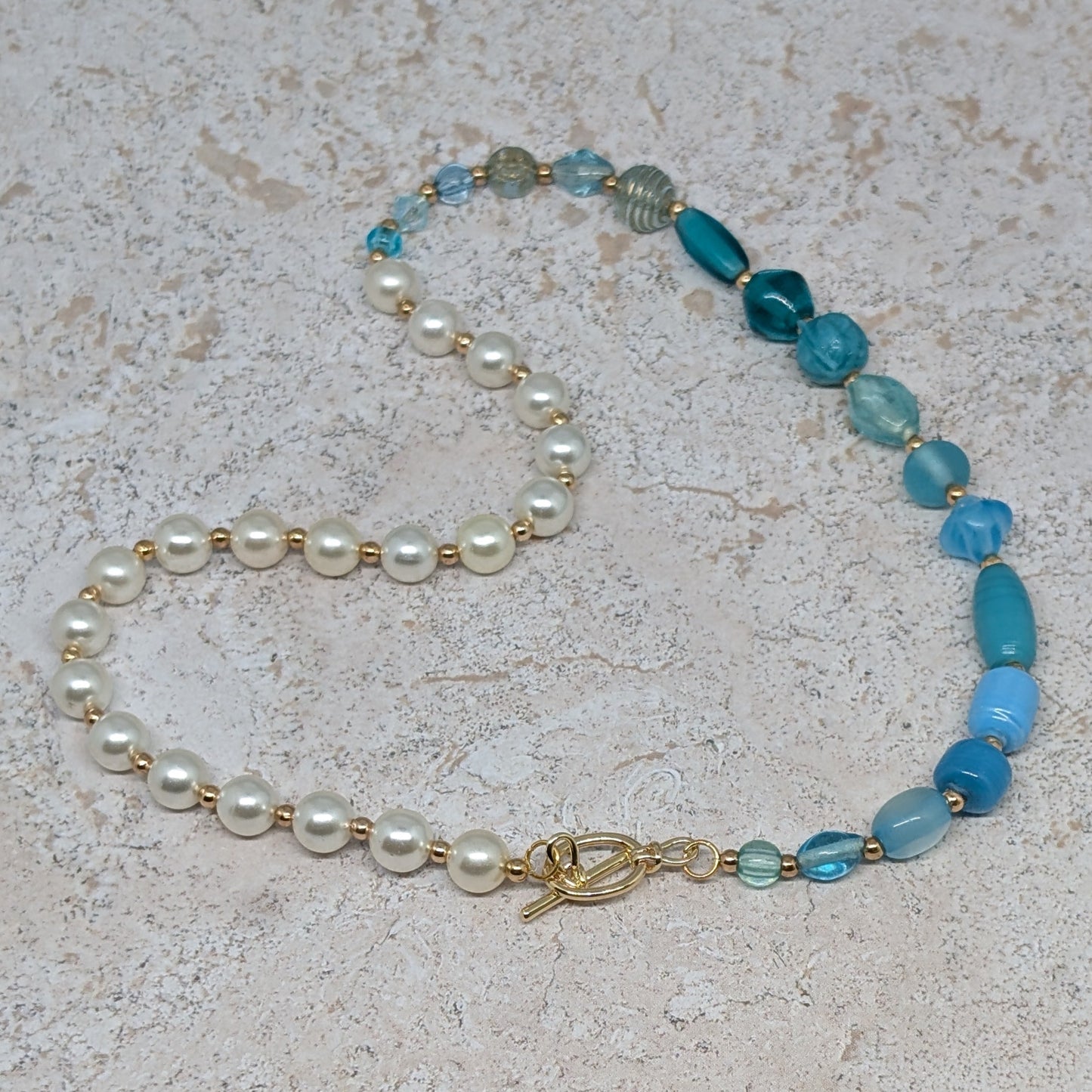 Necklace with pearls and blue beads on a light stone surface
