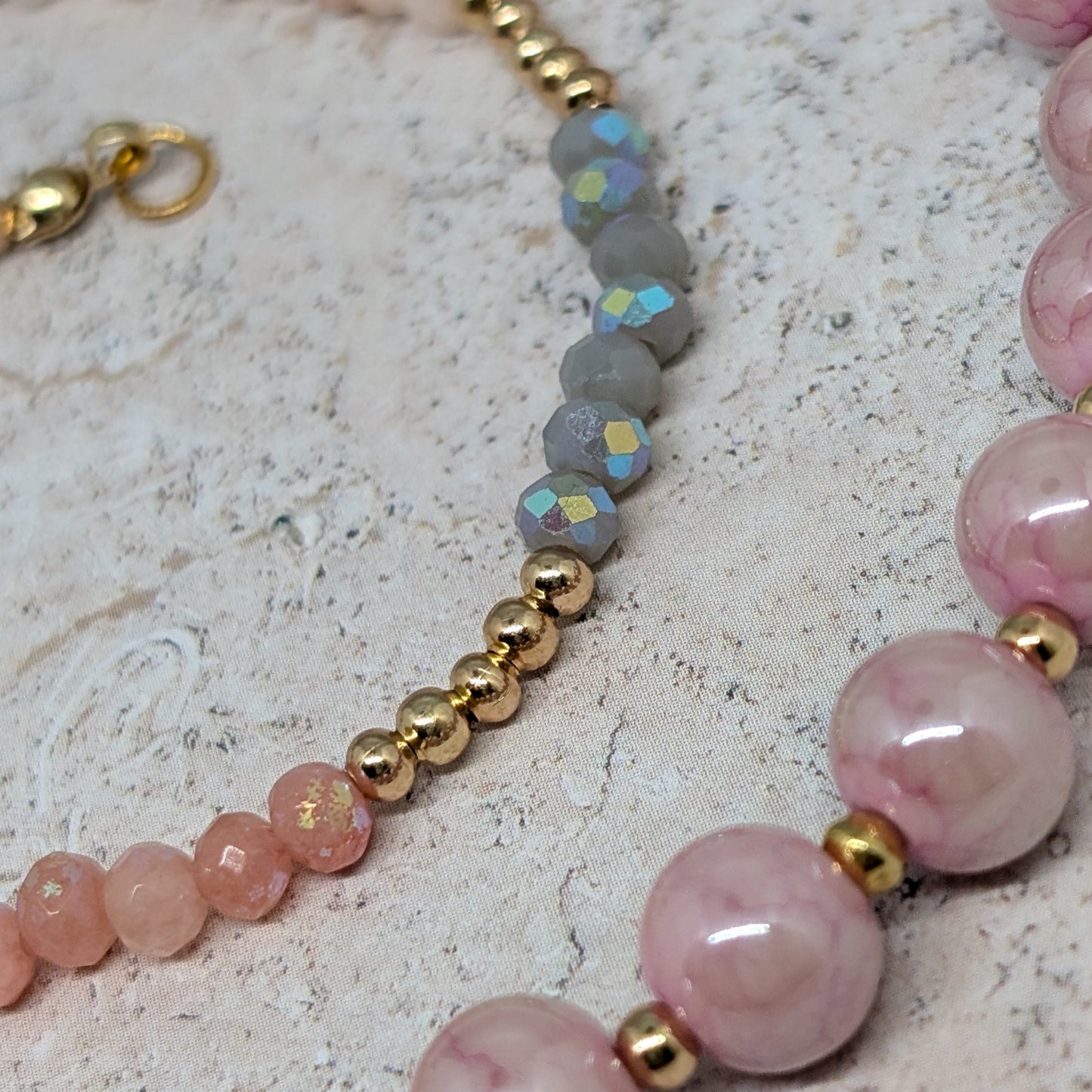 Beaded bracelet with pink beads, gold accents, and opal stones on a textured surface.