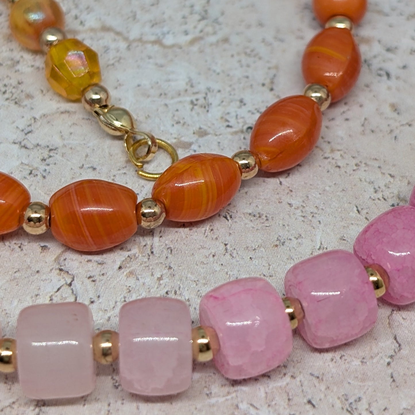Two beaded bracelets with orange, pink, and gold beads on a textured surface.