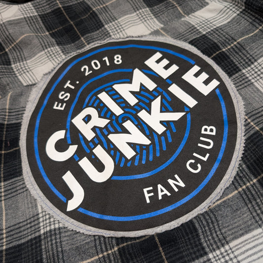 Patch on a plaid fabric with 'Crime Junkie Fan Club' text