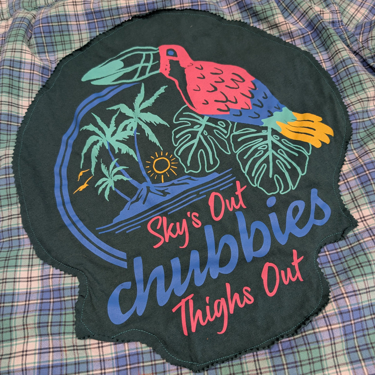Embroidered patch with tropical design and text on a plaid fabric background