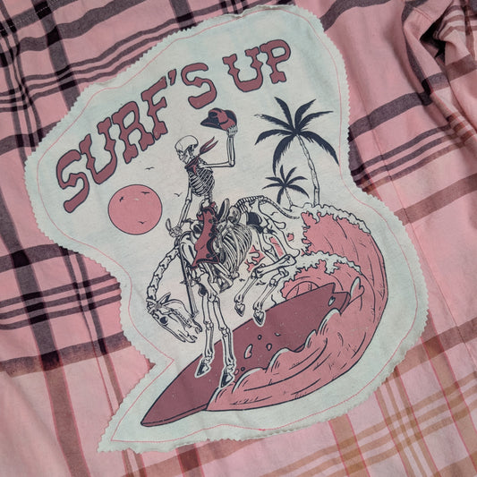 Patch with skeleton surfing and 'Surf's Up' text on a plaid background