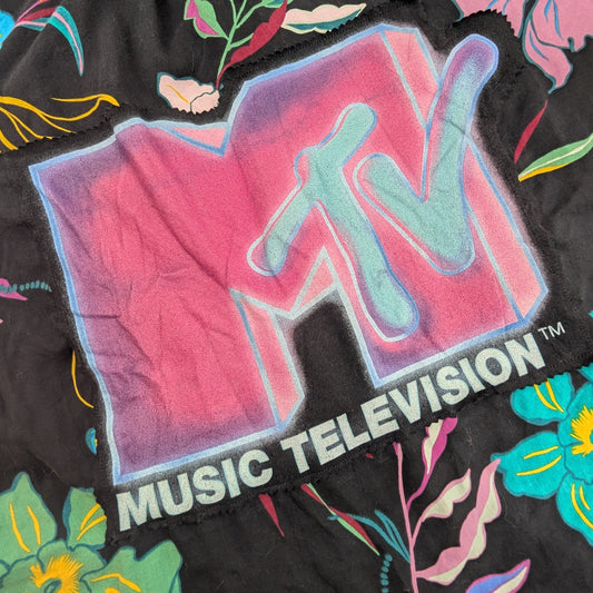 A close-up of a black garment featuring a large, vibrant MTV Music Television logo in pink, purple, and blue, surrounded by a colorful floral print.