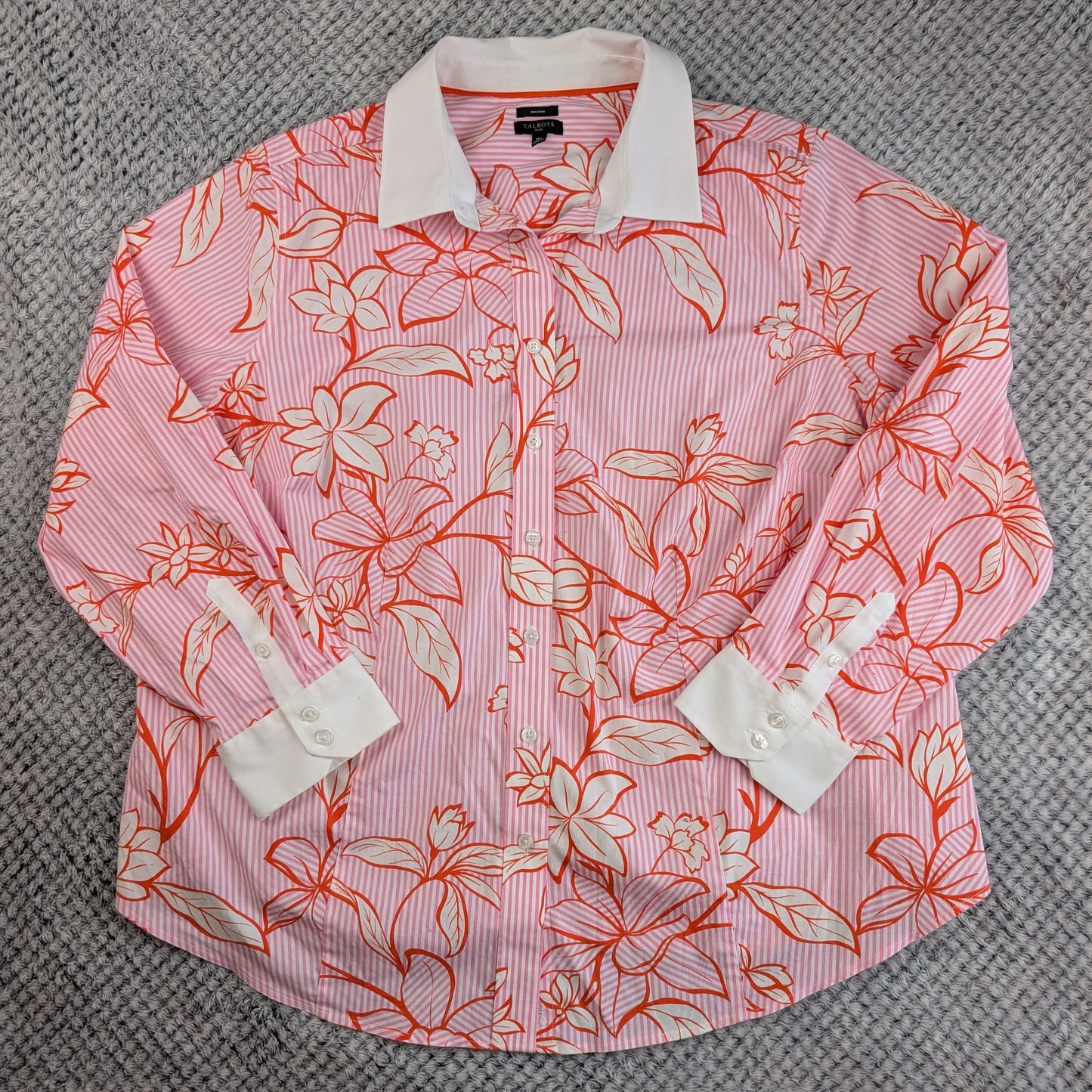 A pink and white striped long-sleeve button-up shirt with a coral orange and white floral print, laid flat on a gray textured carpet.