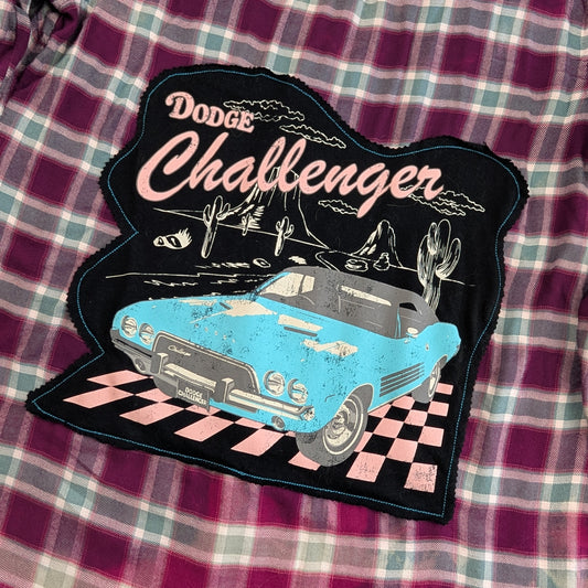 A distressed embroidered patch featuring a light blue Dodge Challenger car and the words 'Dodge Challenger' in pink, placed on a purple and green plaid fabric background.