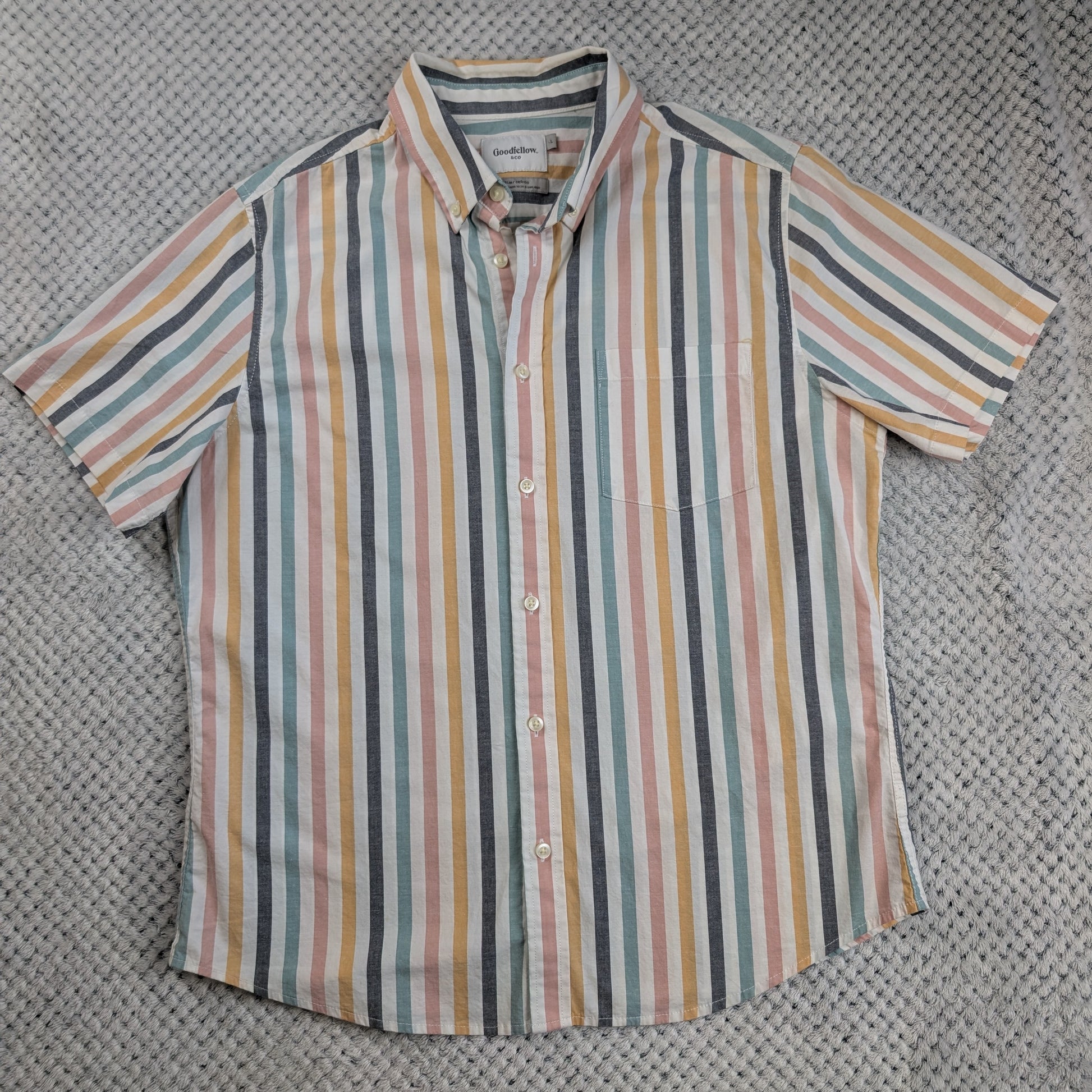 A short-sleeve button-up shirt with vertical pastel stripes in pink, yellow, blue, and gray, laid flat on a textured gray woven surface.