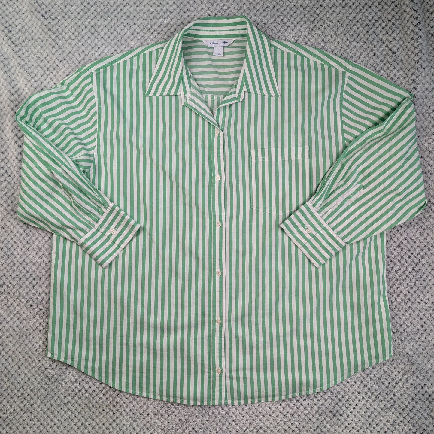 A green and white vertically striped long-sleeve button-up shirt laid flat on a textured gray knit blanket.