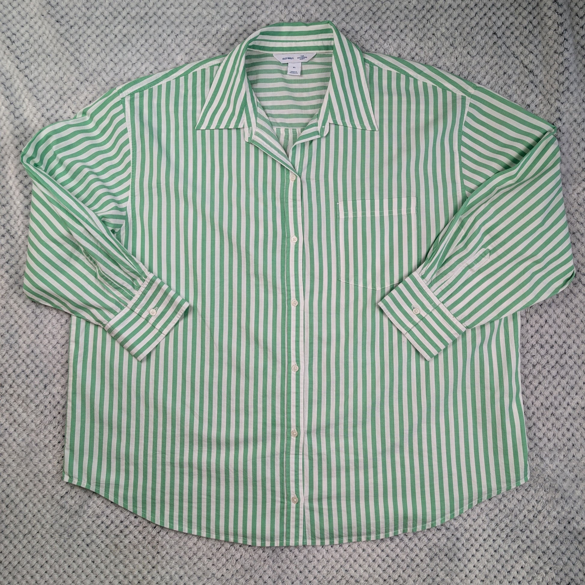 A green and white vertically striped long-sleeve button-up shirt laid flat on a textured gray knit blanket.