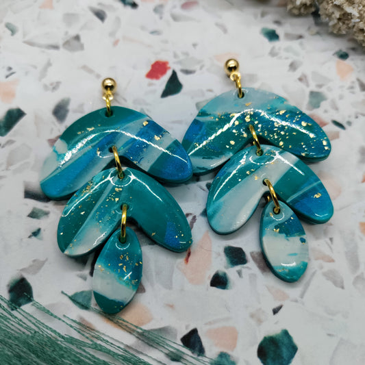 Pair of blue leaf-shaped earrings with gold accents on a patterned surface