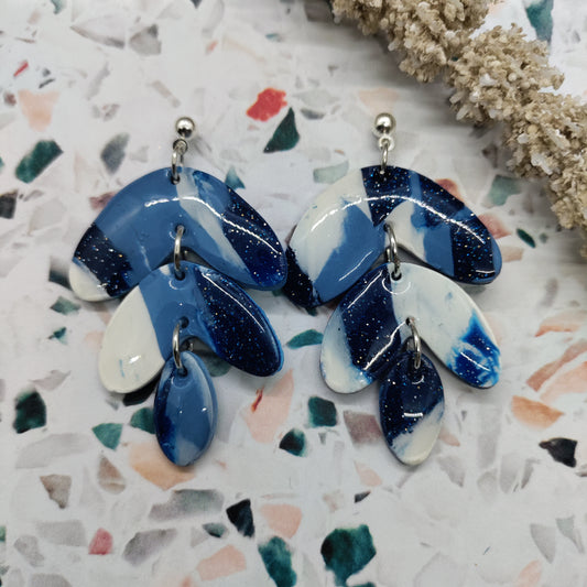 Pair of blue and white earrings on a terrazzo surface with coral.