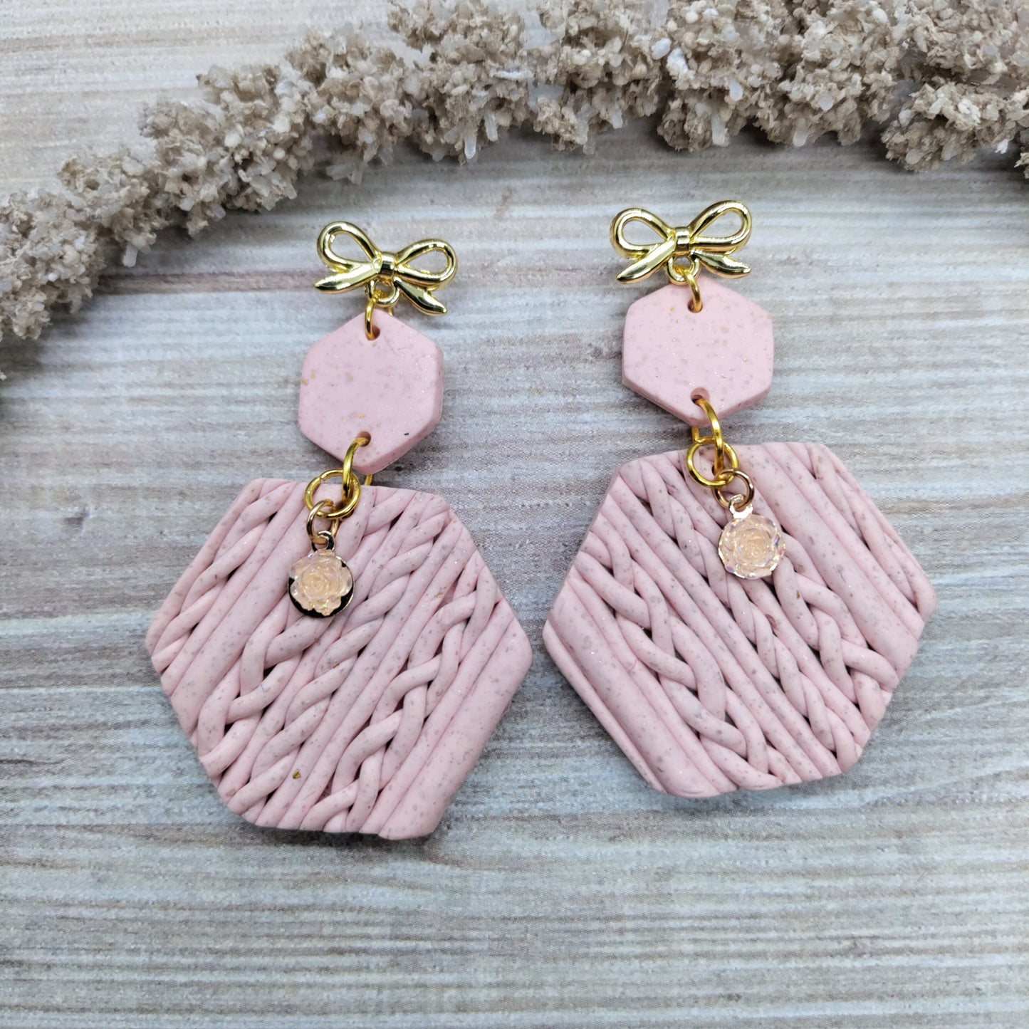 Pink earrings with gold accents on a textured surface