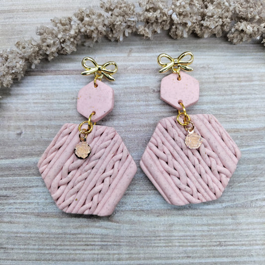 Pink earrings with gold accents on a textured surface