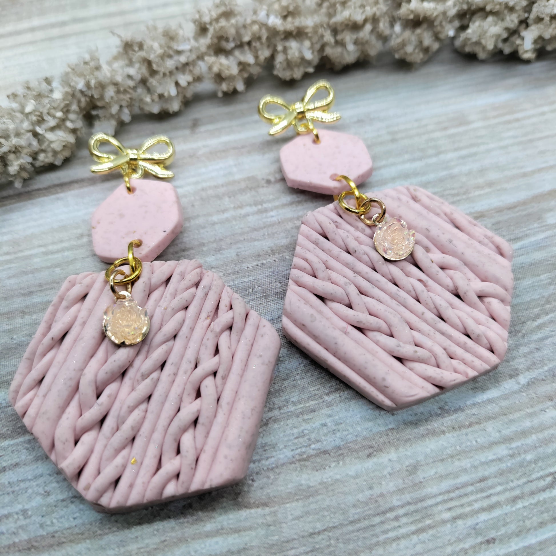 Pink textured earrings with gold accents on a wooden surface