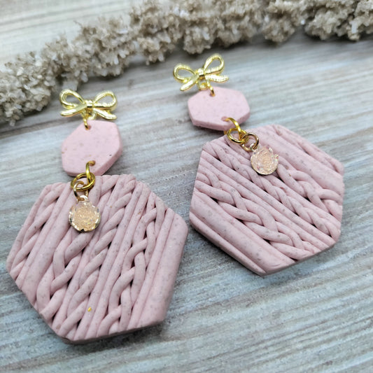 Pink textured earrings with gold accents on a wooden surface