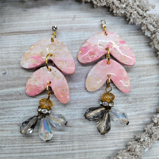 Pair of pink earrings with gold and crystal accents on a textured surface.