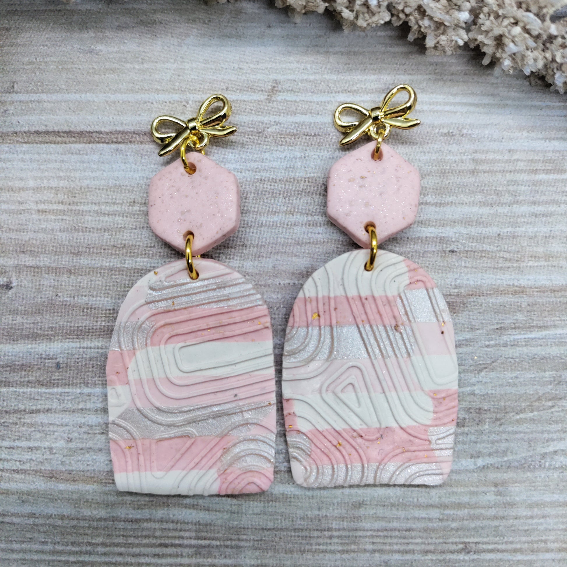 Pair of earrings with pink and white marbled design on a textured surface