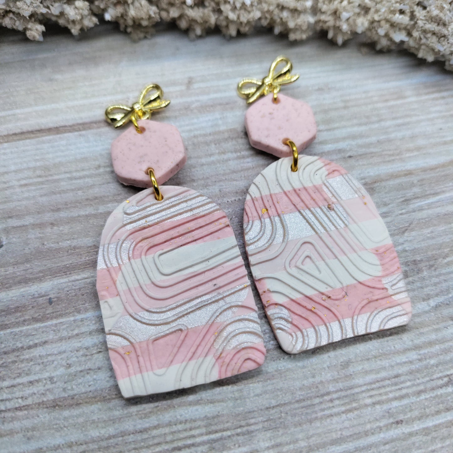 Pink and white marbled earrings with gold bows on a wooden surface