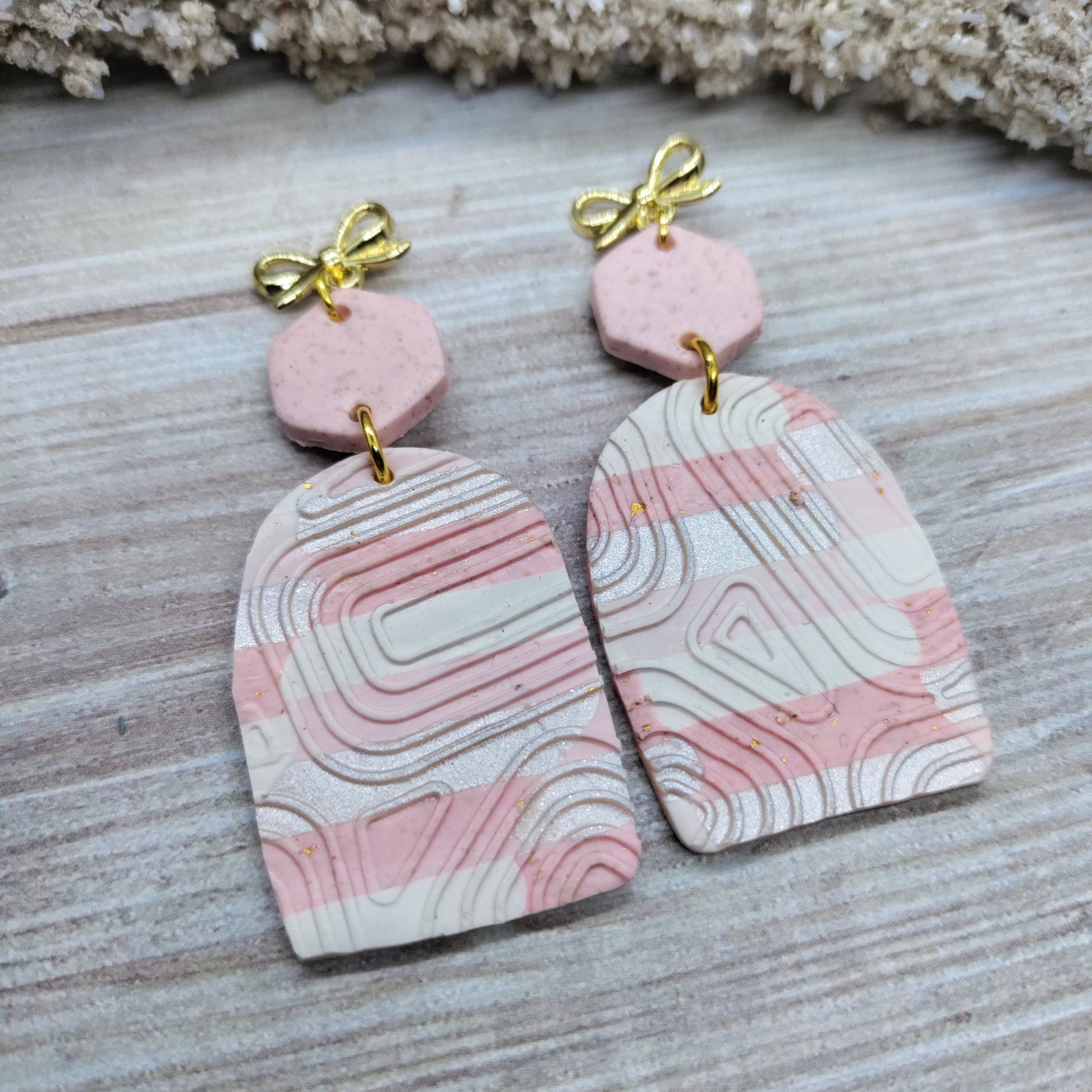 Pink and white marbled earrings with gold bows on a wooden surface