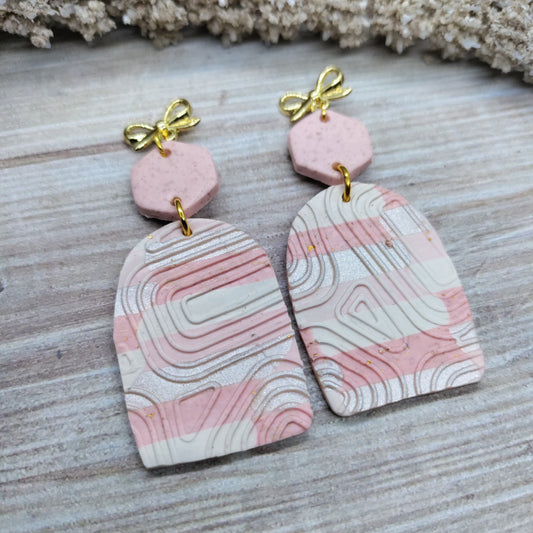 Pink and white marbled earrings with gold bows on a wooden surface