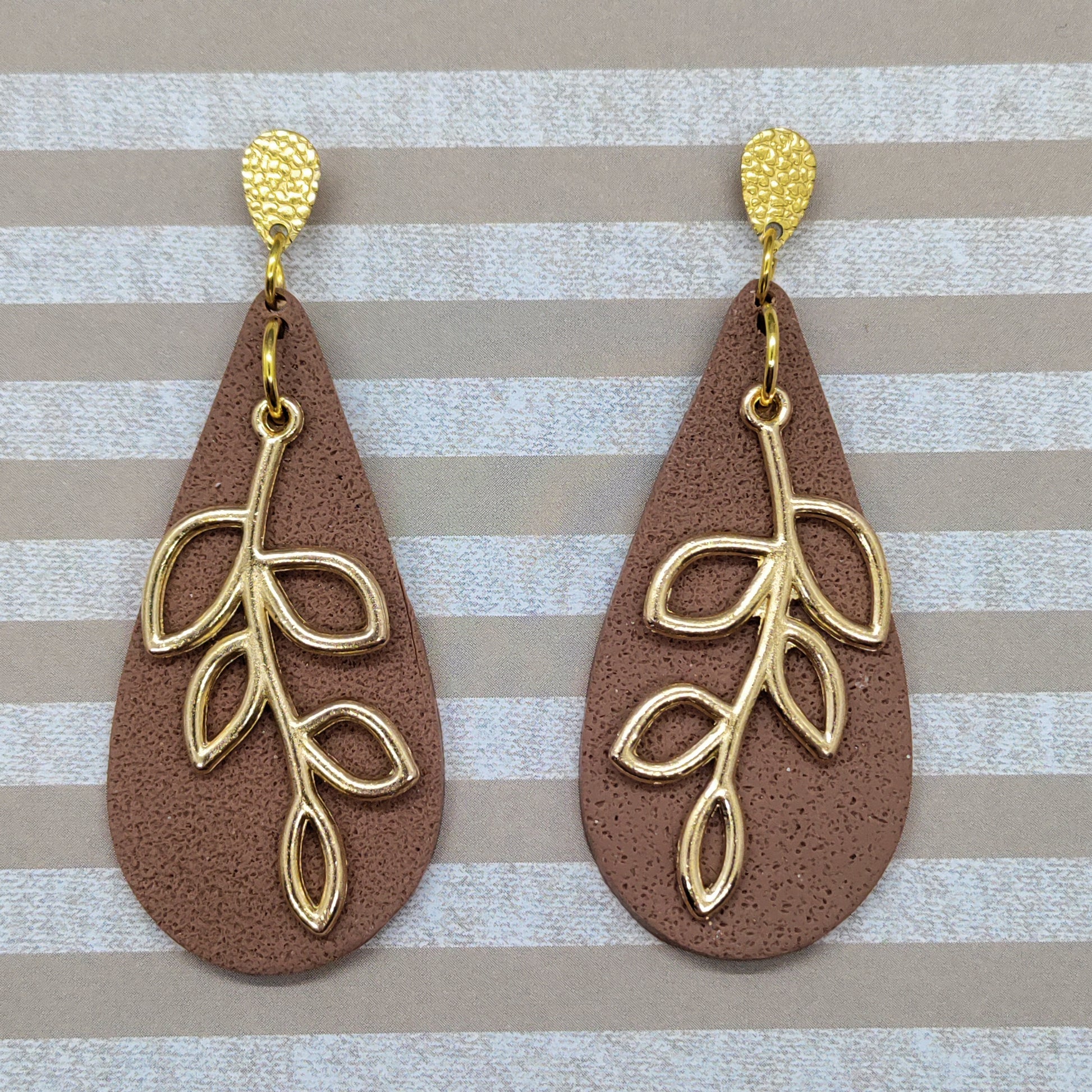 Pair of brown teardrop earrings with gold leaf designs on a striped background