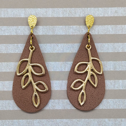 Pair of brown teardrop earrings with gold leaf designs on a striped background