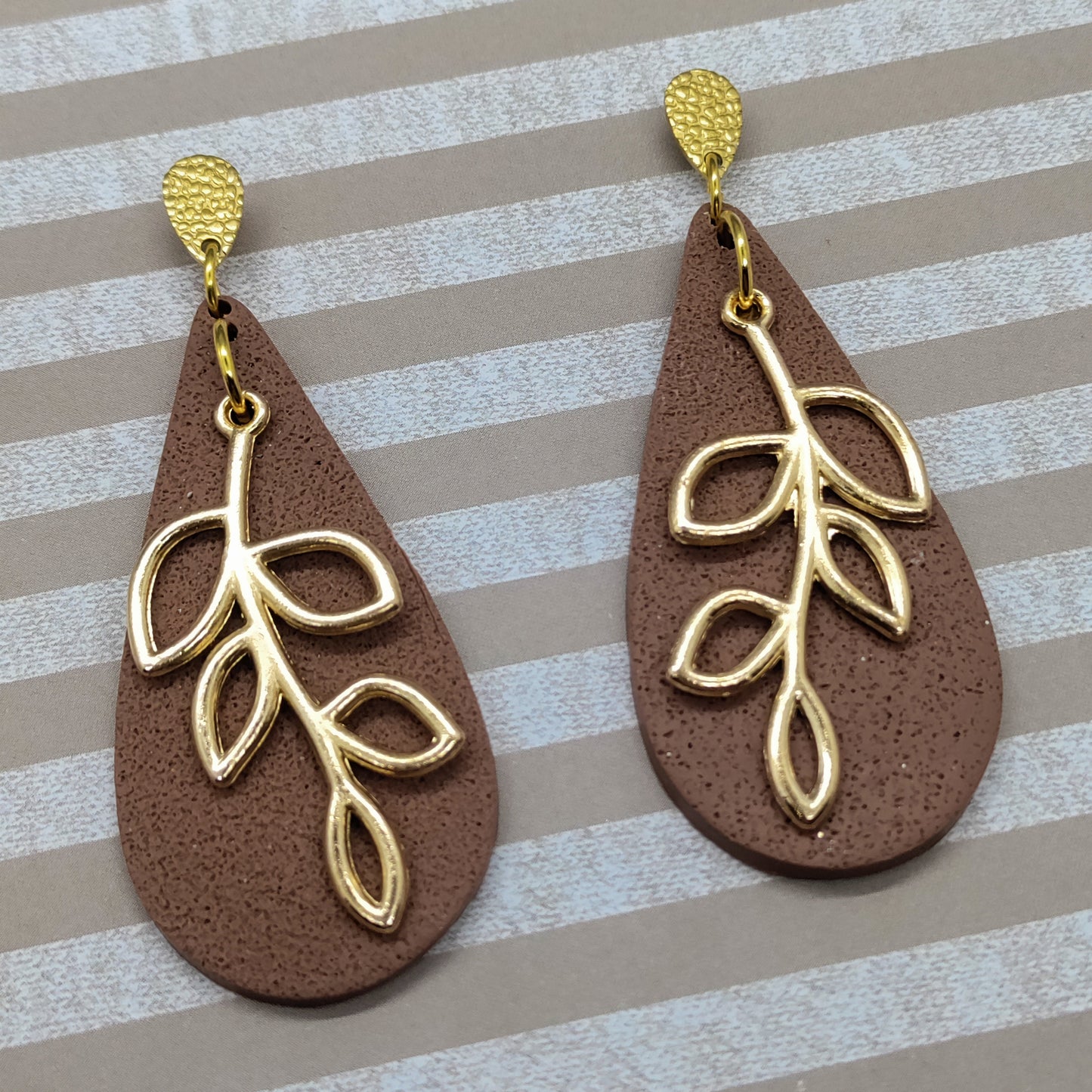 Brown teardrop earrings with gold leaf designs on a striped background