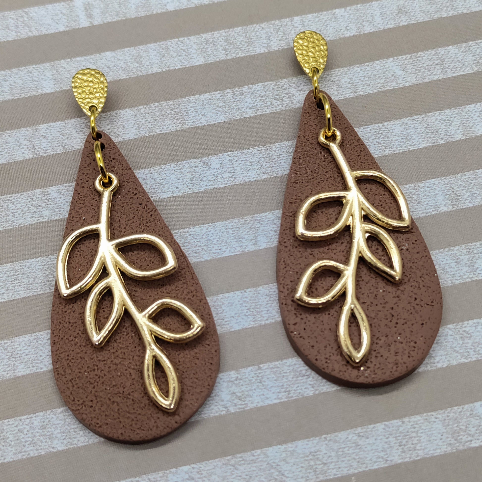 Brown teardrop earrings with gold leaf designs on a striped background