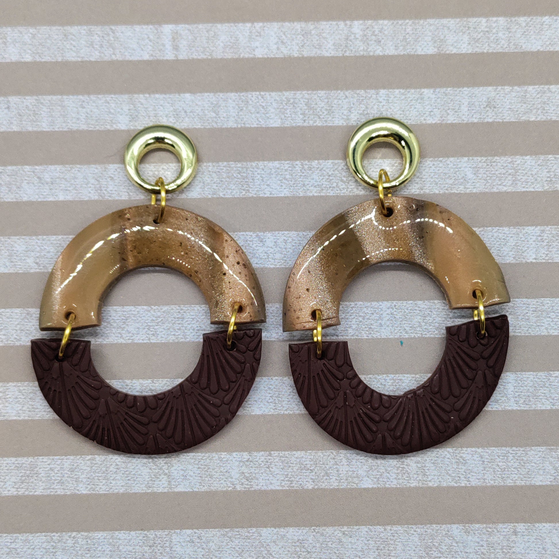 Pair of gold and brown earrings on a striped background