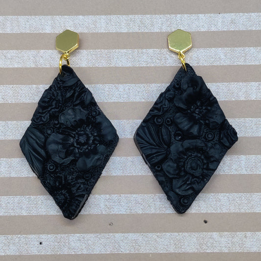 Black floral earrings with gold hooks on a striped background
