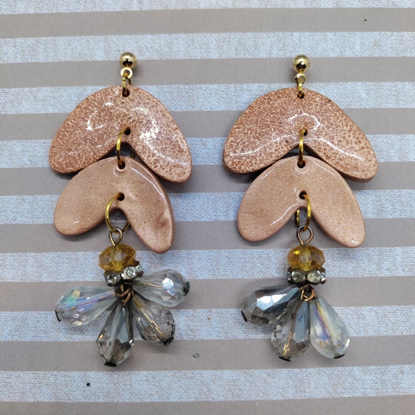 Pair of ceramic earrings with beaded drops on a striped background