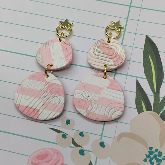 Pair of pink and gold earrings on a lined paper background with floral design.