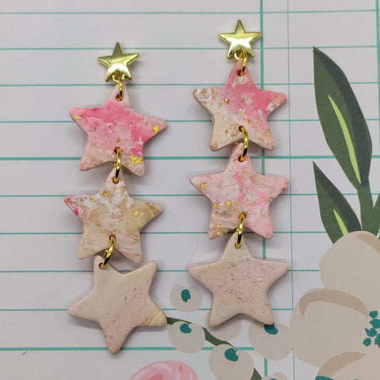 Star-shaped earrings with pink and gold accents on a floral and grid background