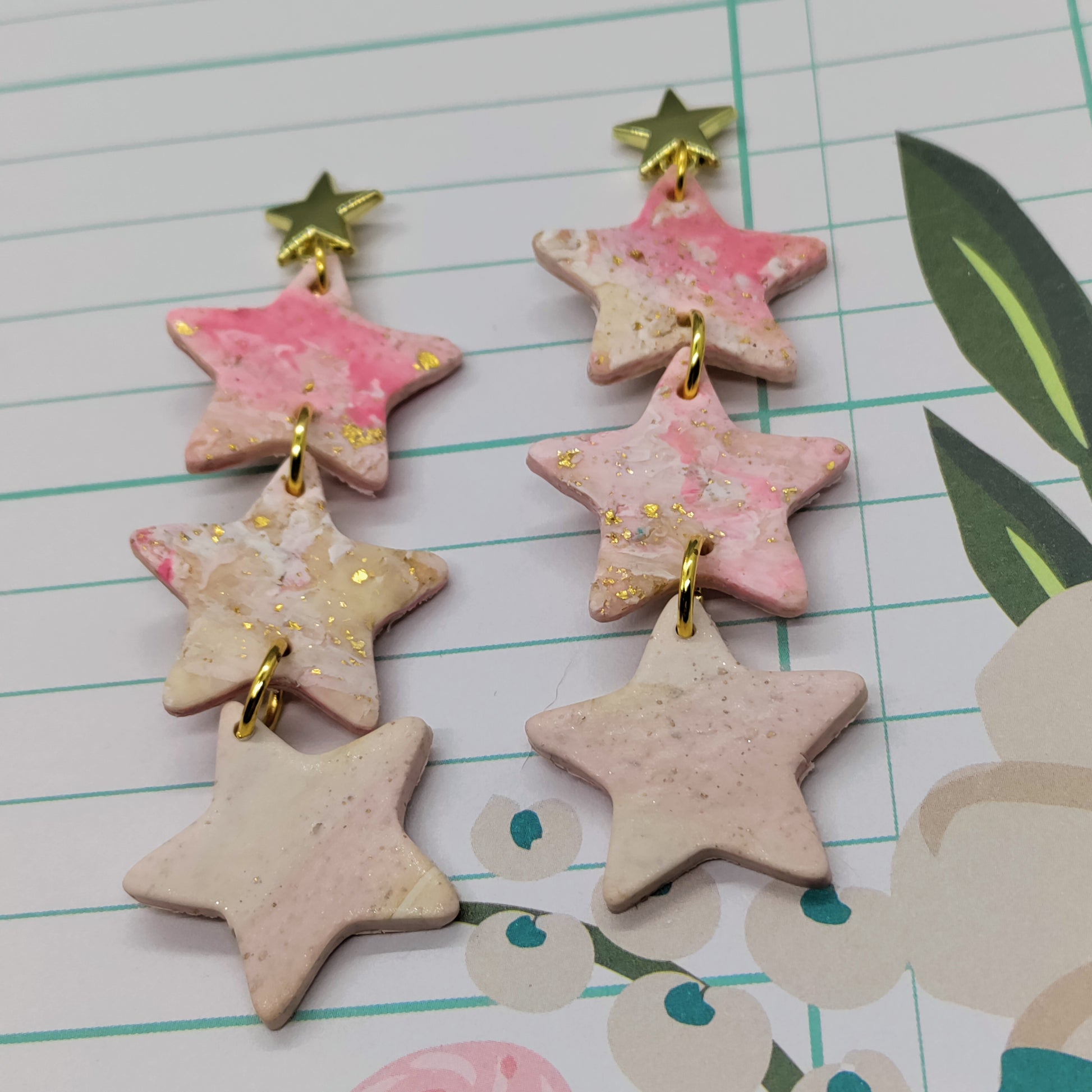 Star-shaped earrings with pink and gold accents on a lined paper background