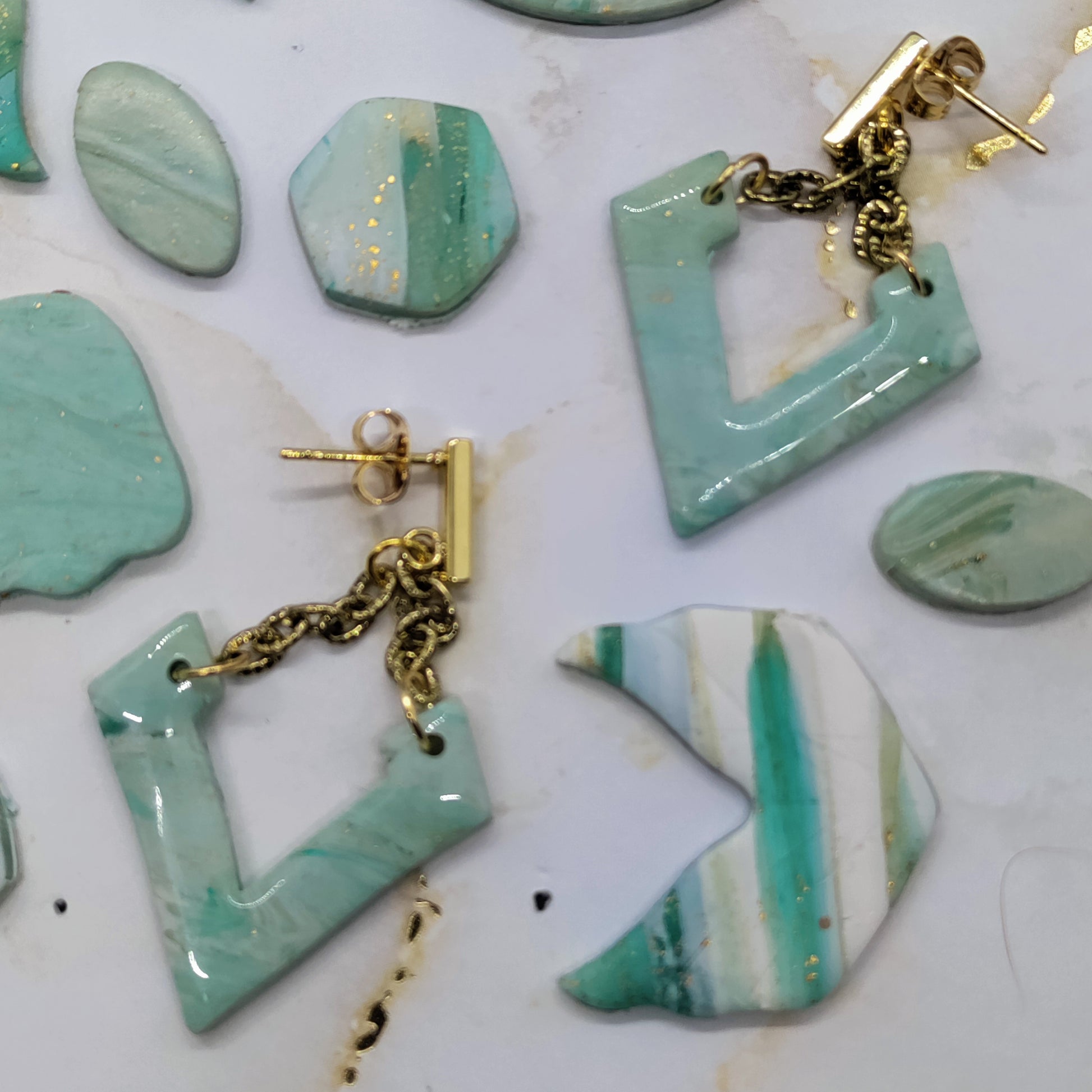 Turquoise ceramic earrings with gold chains on a white surface