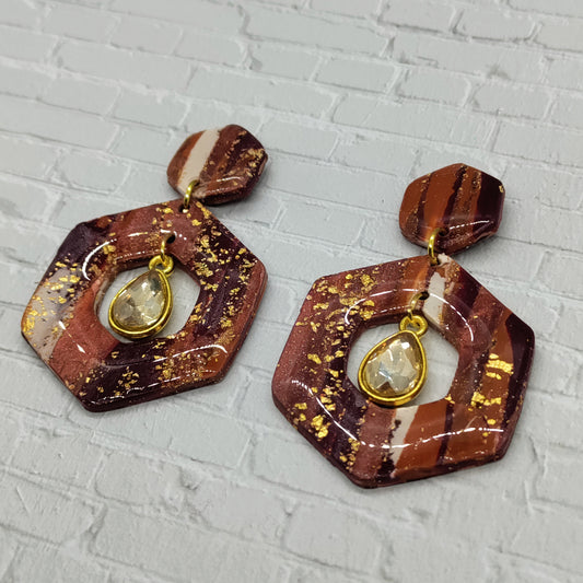 Hexagonal brown earrings with gold accents on a textured gray background
