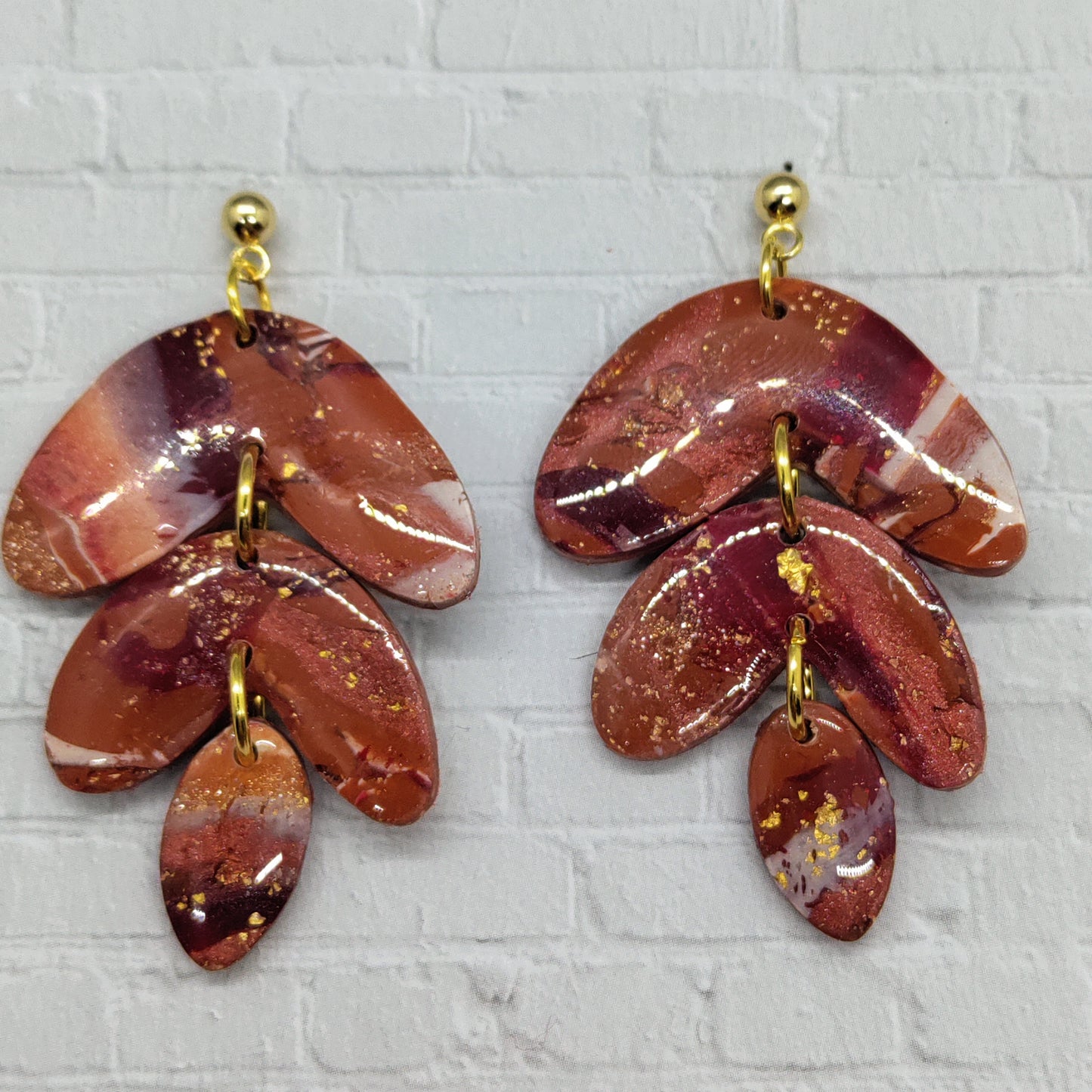Pair of red and gold leaf-shaped earrings on a textured gray background
