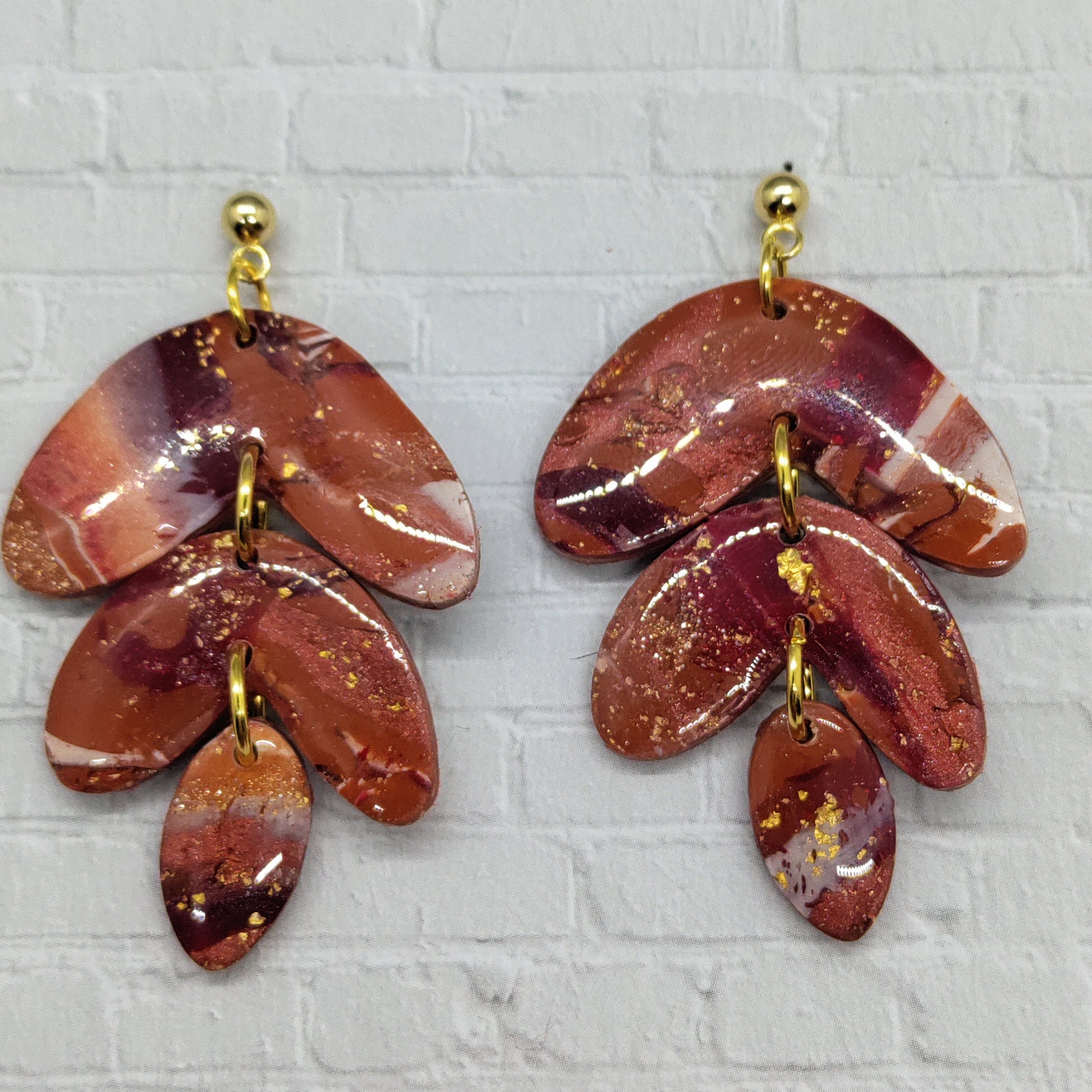 Pair of red and gold leaf-shaped earrings on a textured gray background