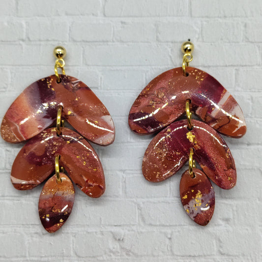Pair of red and gold leaf-shaped earrings on a textured gray background