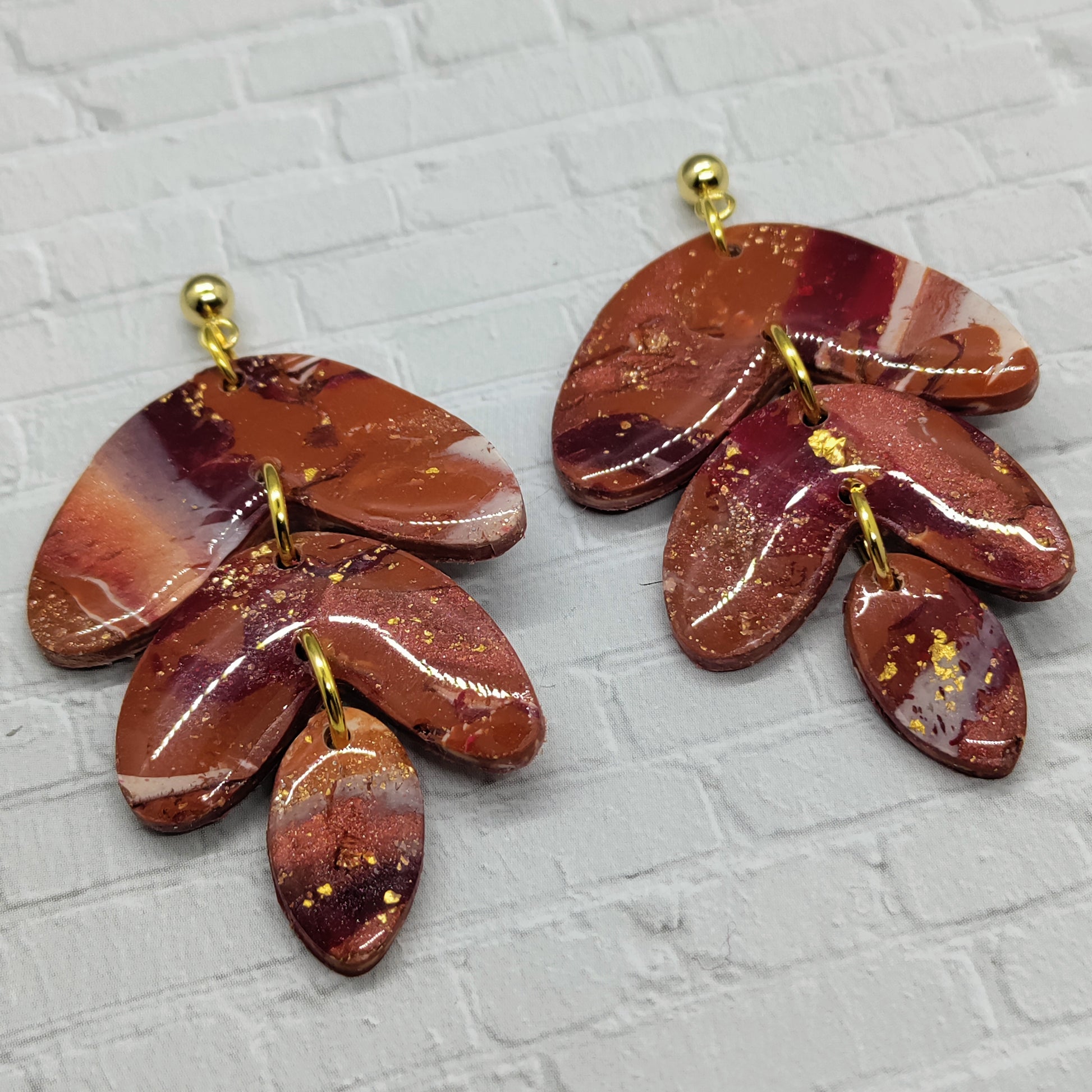 Pair of brown and gold leaf-shaped earrings on a textured gray background